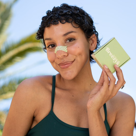 Girl wearing a sage green floral Breezys Nasal Strip and holding the matching packaging with a gentle smile.