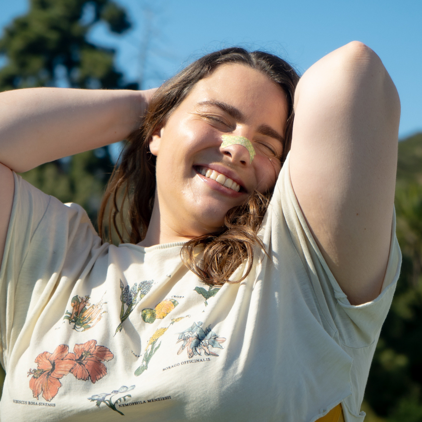 Girl wearing a sage green floral nasal strip while stretching her arms above her taking in the summer sun and fresh air.